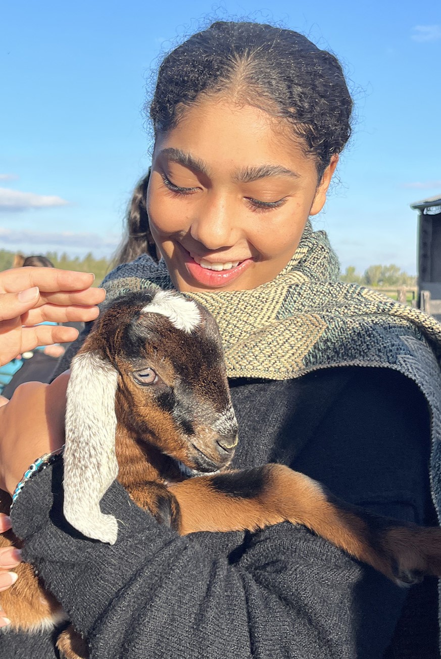 A student, outdoors, holding a young goat.