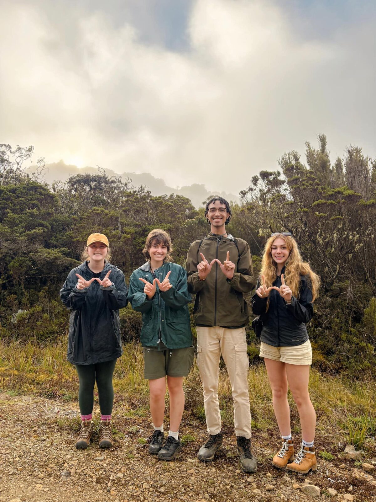 Four students making a "W" with their fingers while standing in front of trees.
