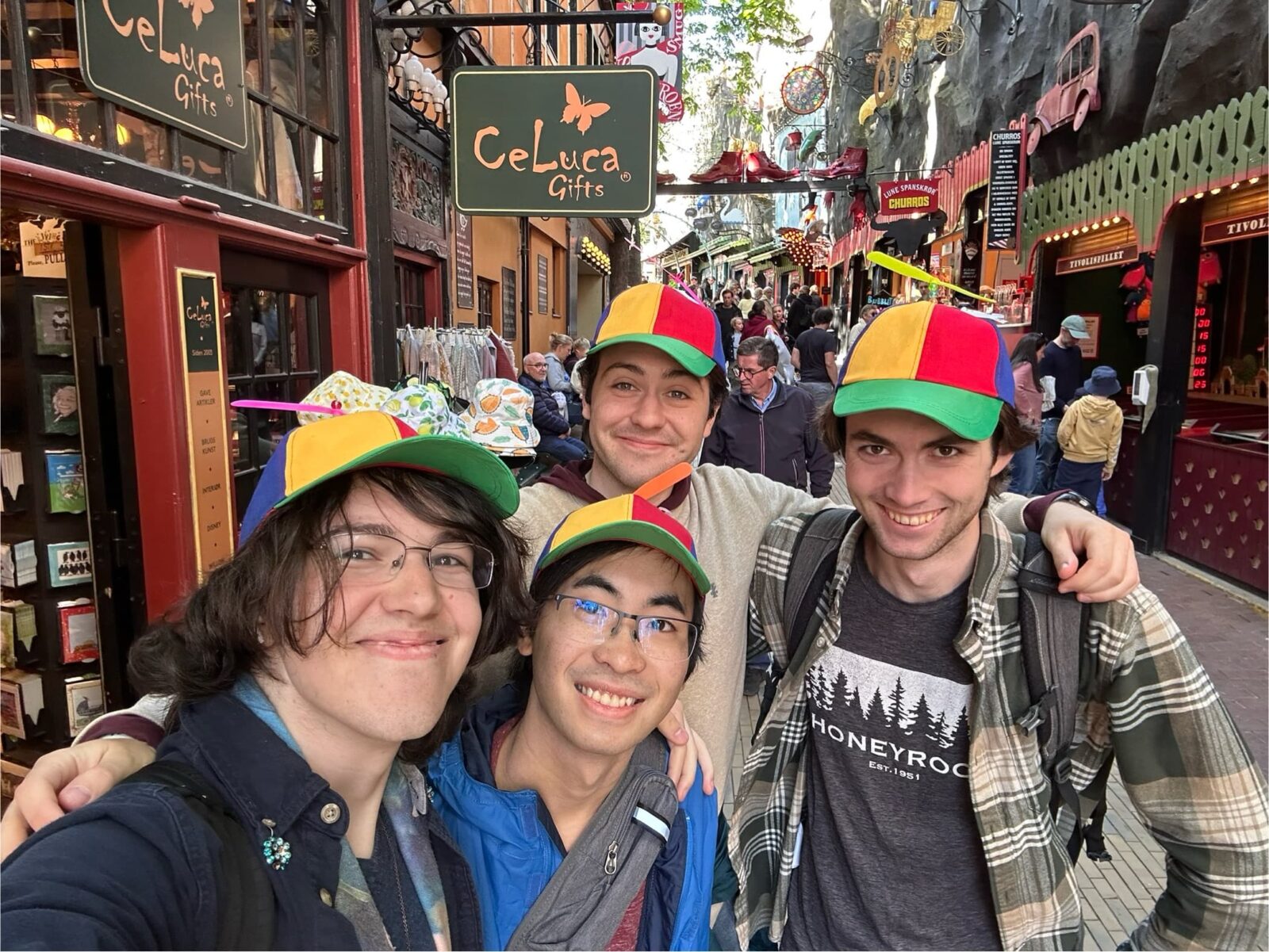 Four students, wearing colorful hats, posing in a busy pedestrian walkway.