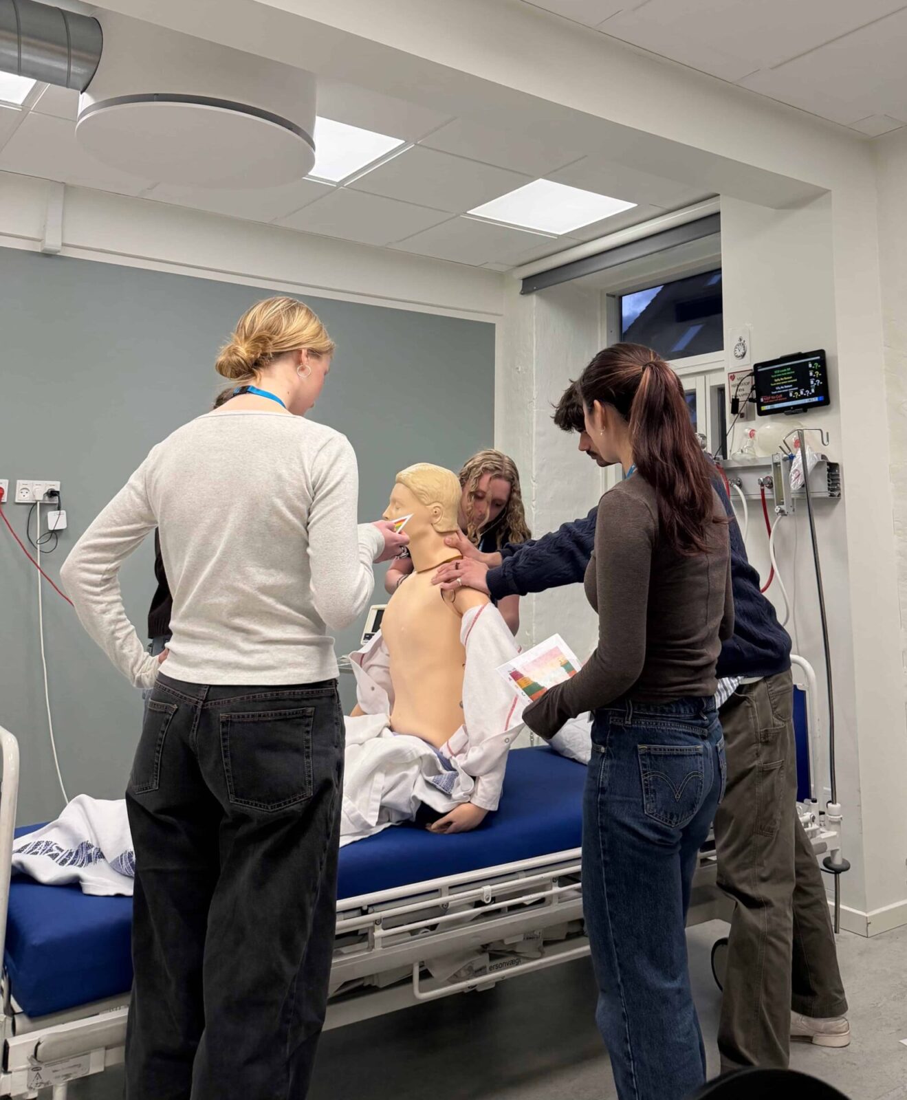 Students stand around a gurney and interact with a medical mannequin.
