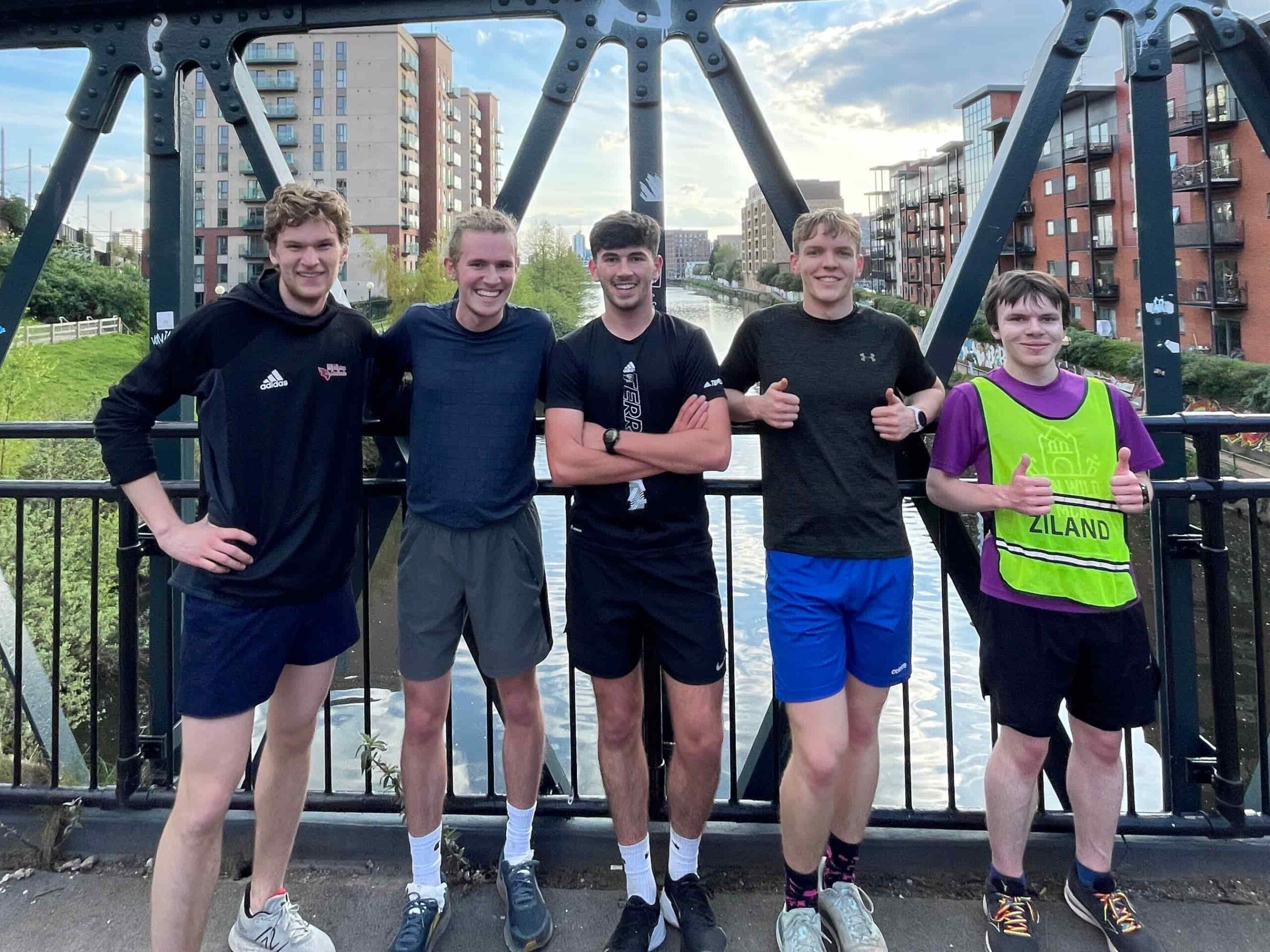 Five students in running clothes, posing on a bridge over a canal.