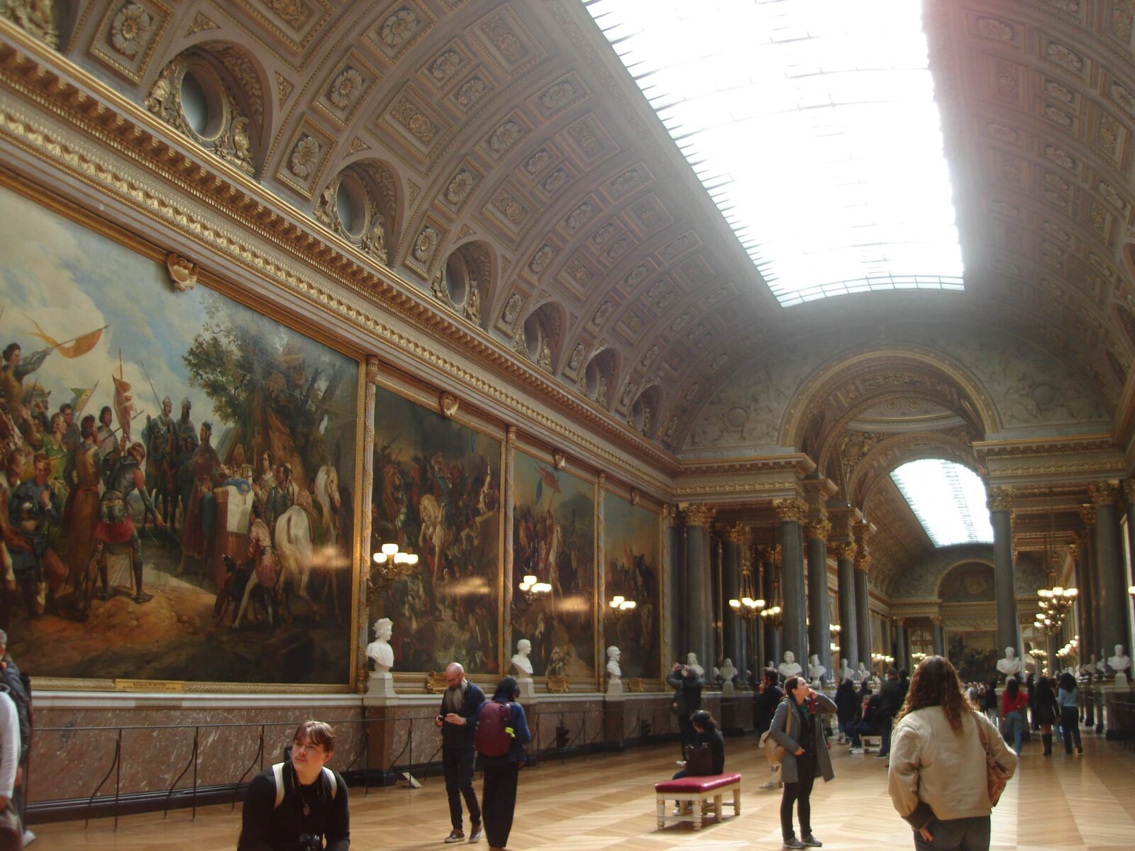 A large ornate hall lined with classical oil paintings and people admiring it.