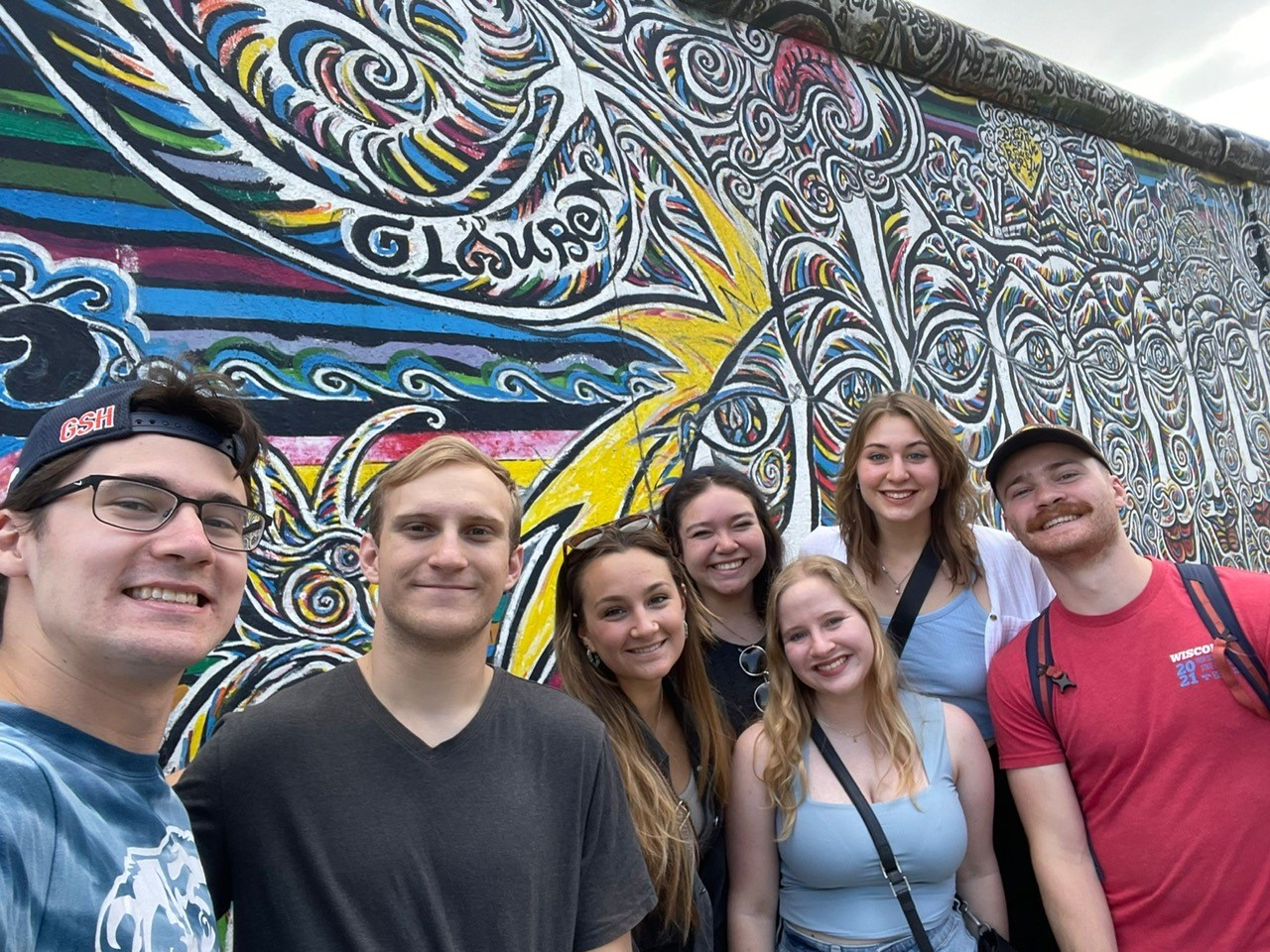 Seven students posing for a picture along a brightly painted wall.