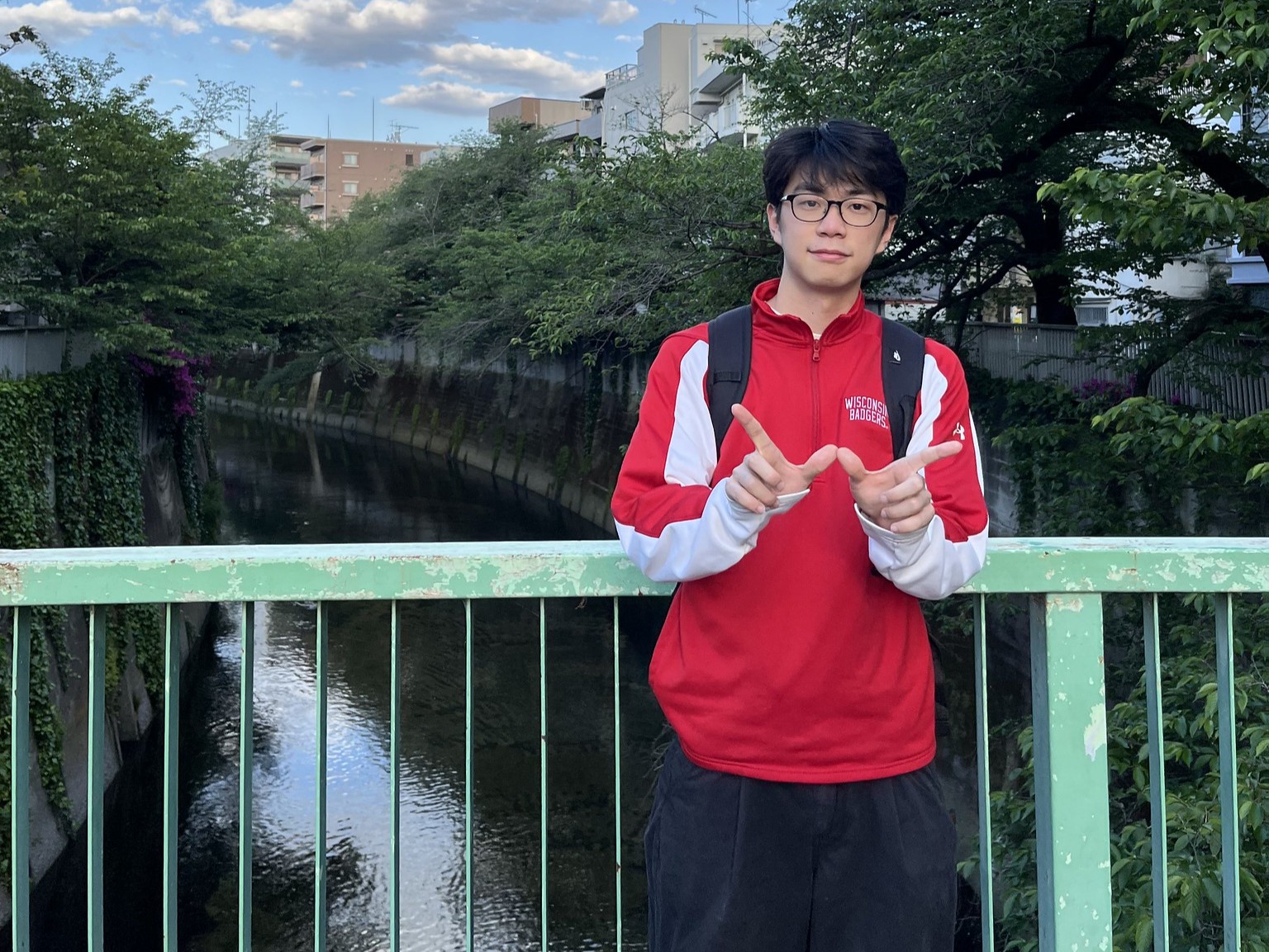 A student posing on a bridge over a canal, making a "W" with their fingers. 