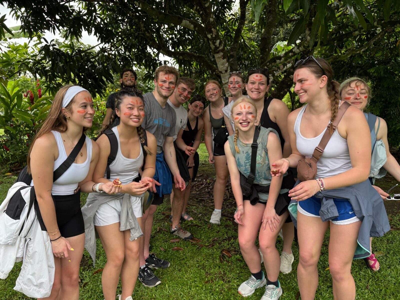 A group of students standing under a tree, with orange face paint on their faces.