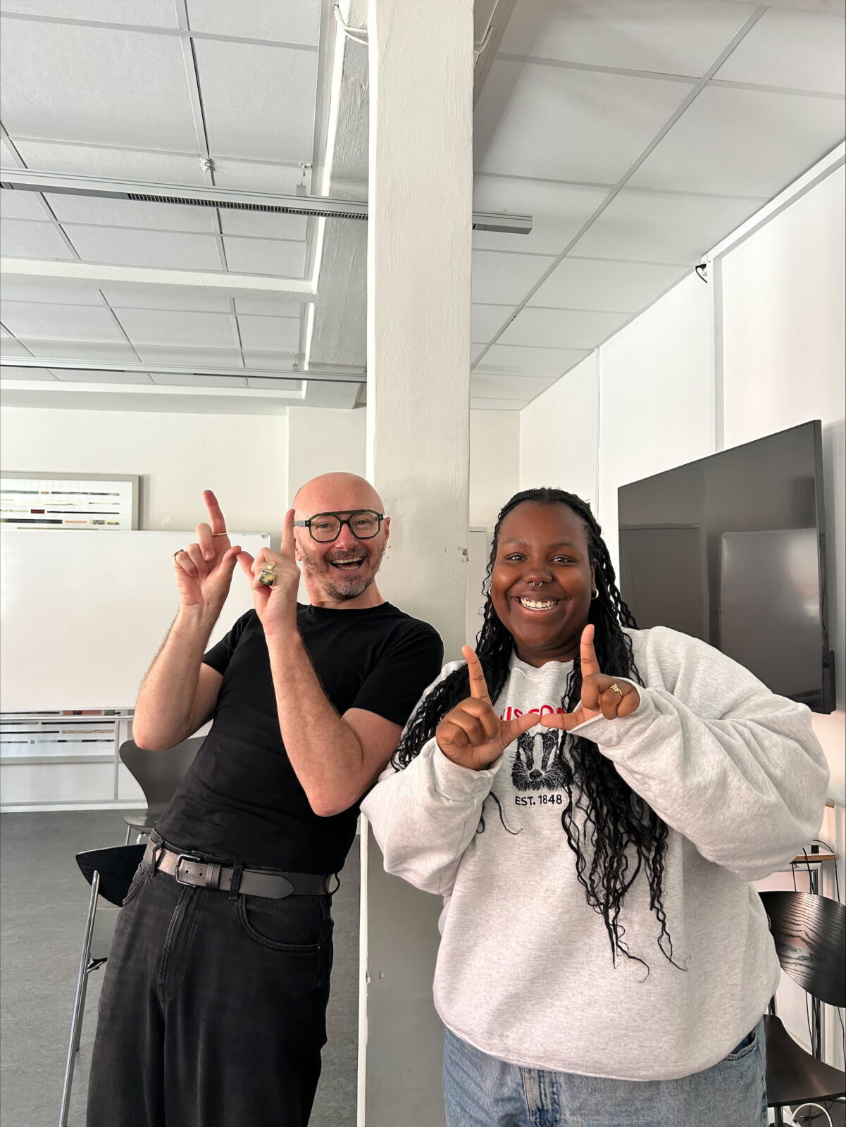 A student and professor posing in a classroom, both holding up finger Ws.