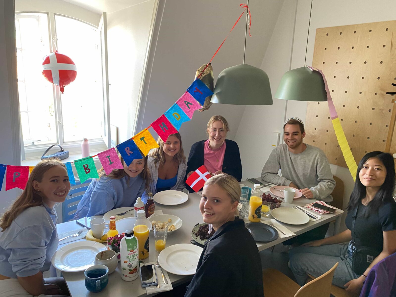 Seven students sitting around a table, with large plates and glasses of juice, and birthday decorations on the ceiling.