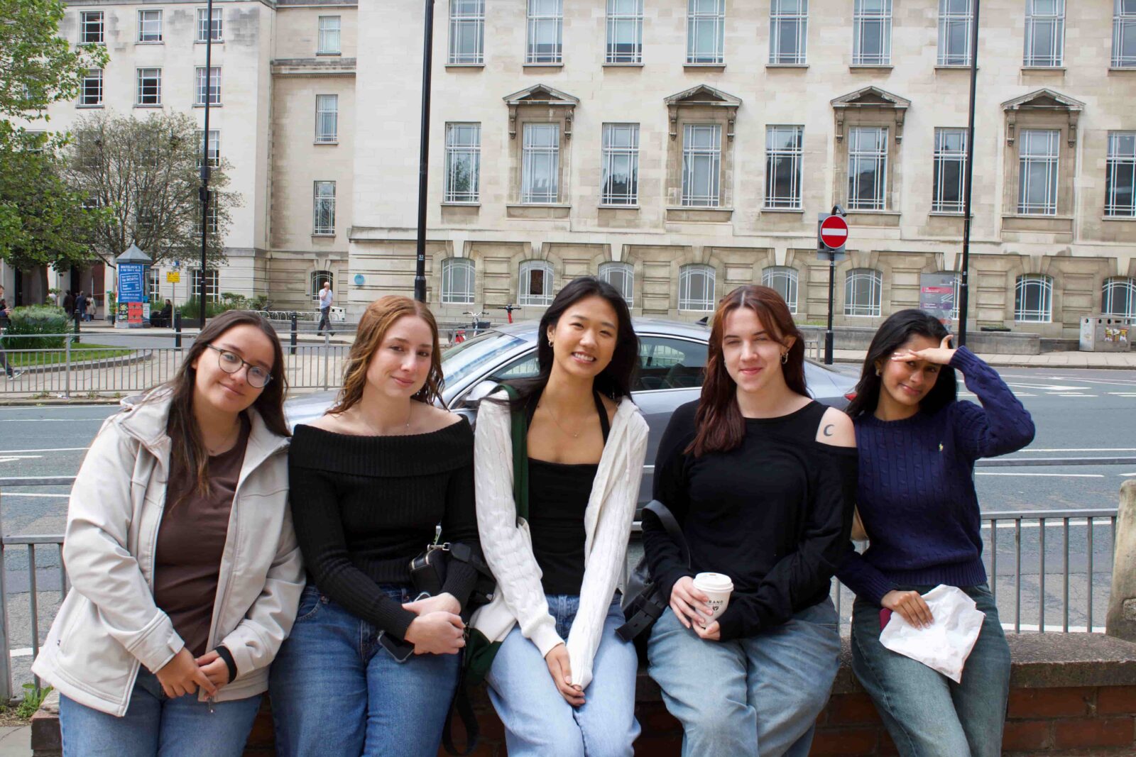 Five students on a sidewalk bench, posing.