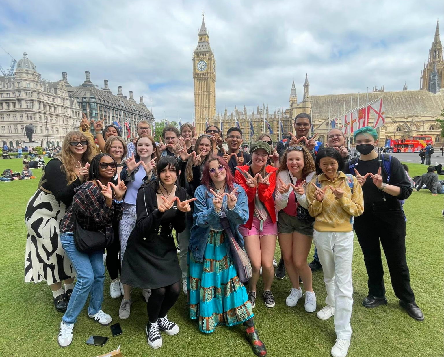 A group of students posing on a grassy square in front of the Big Ben clock tower, holding up finger Ws.