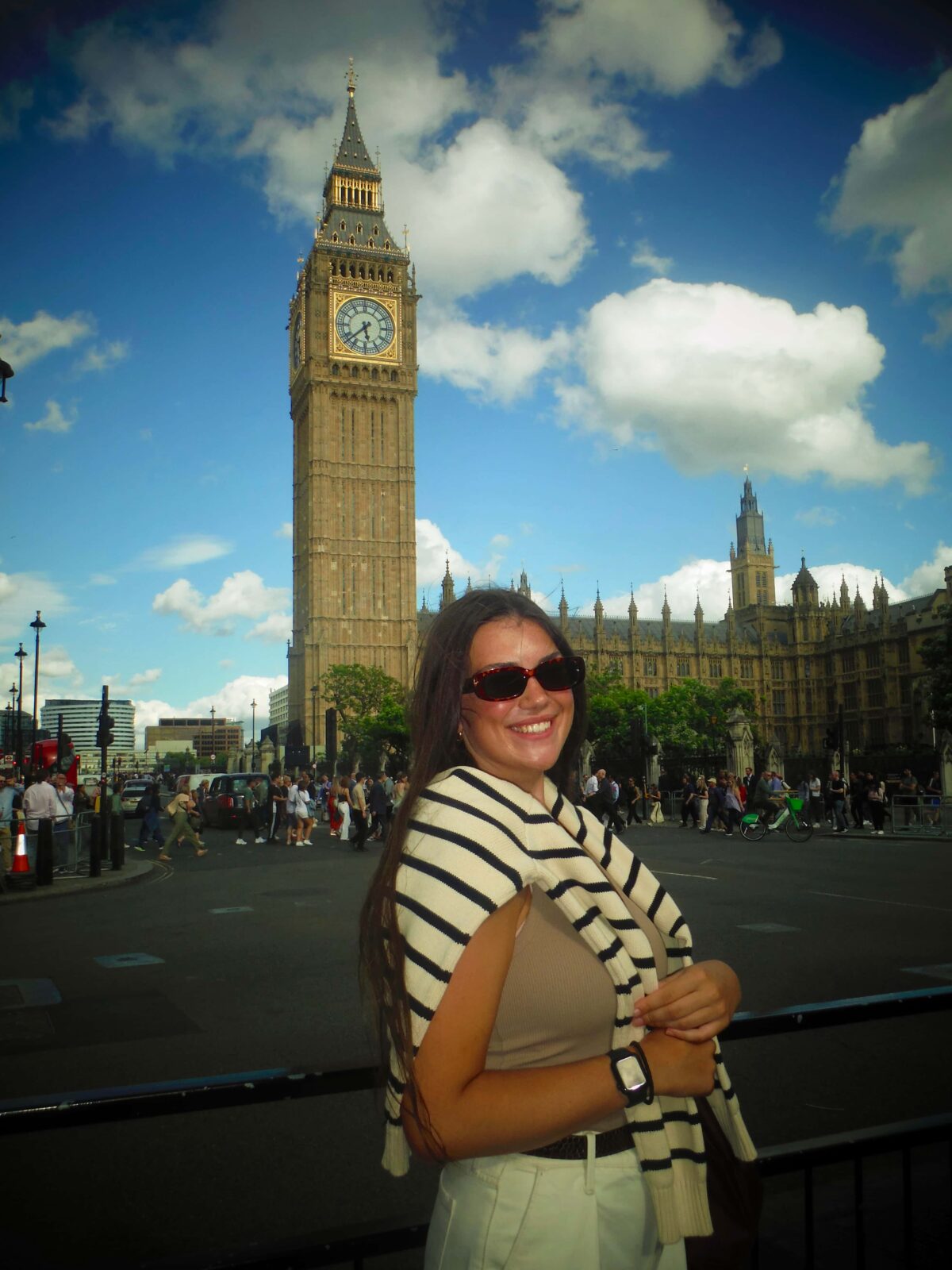 A student posing in front of Big Ben on a sunny day, looking at the camera, smiling.