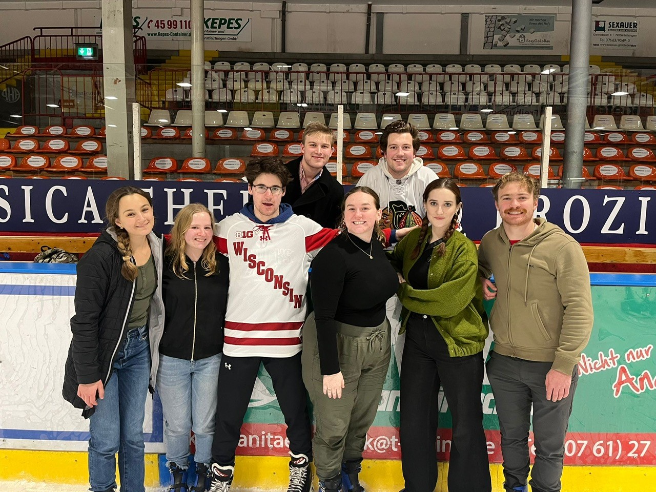 Students skating at an ice rink, posing for a group photo.