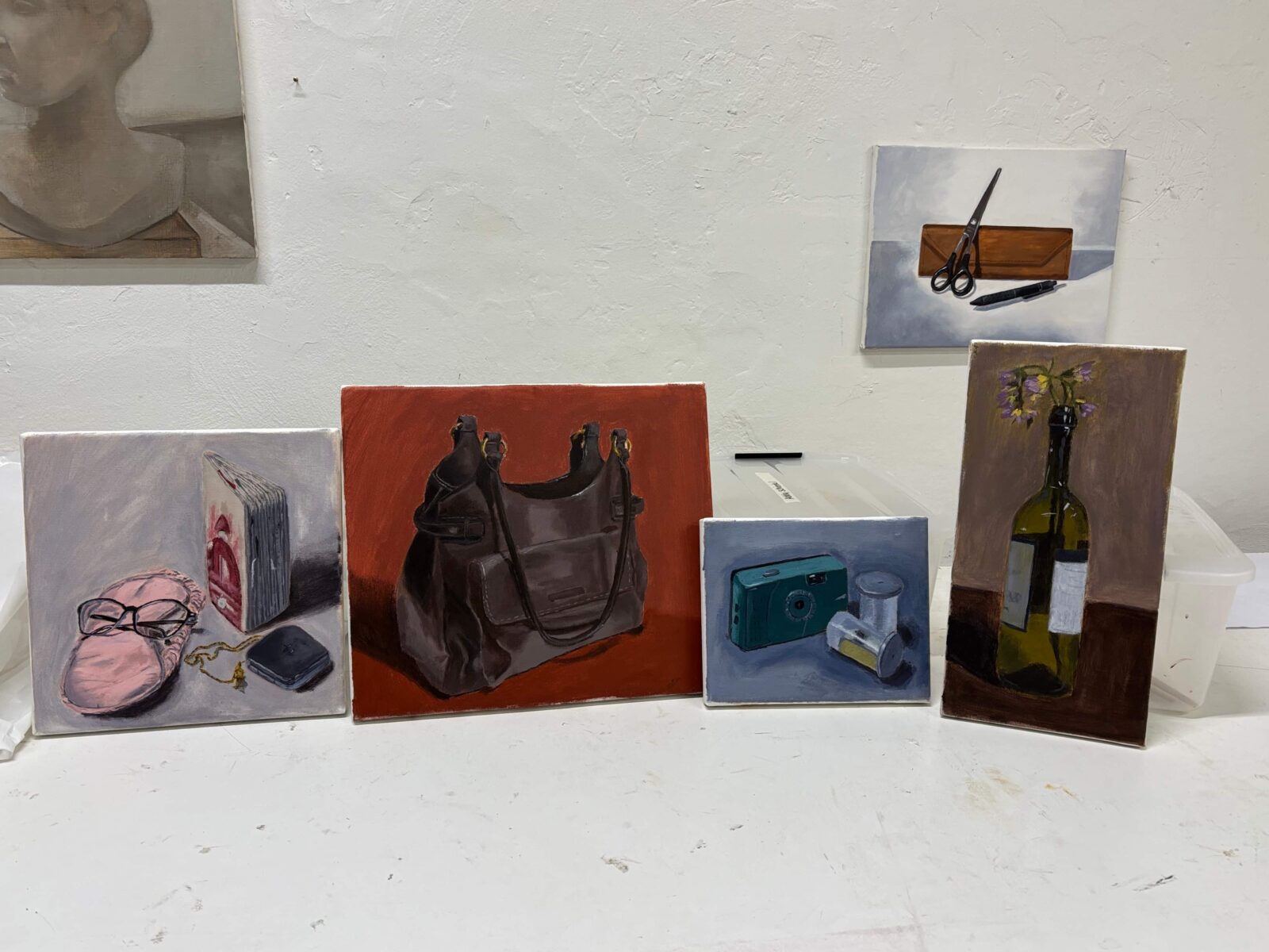 Five painted canvases of everyday objects, including one of a purse, one of a camera, and one of flowers in a glass bottle.