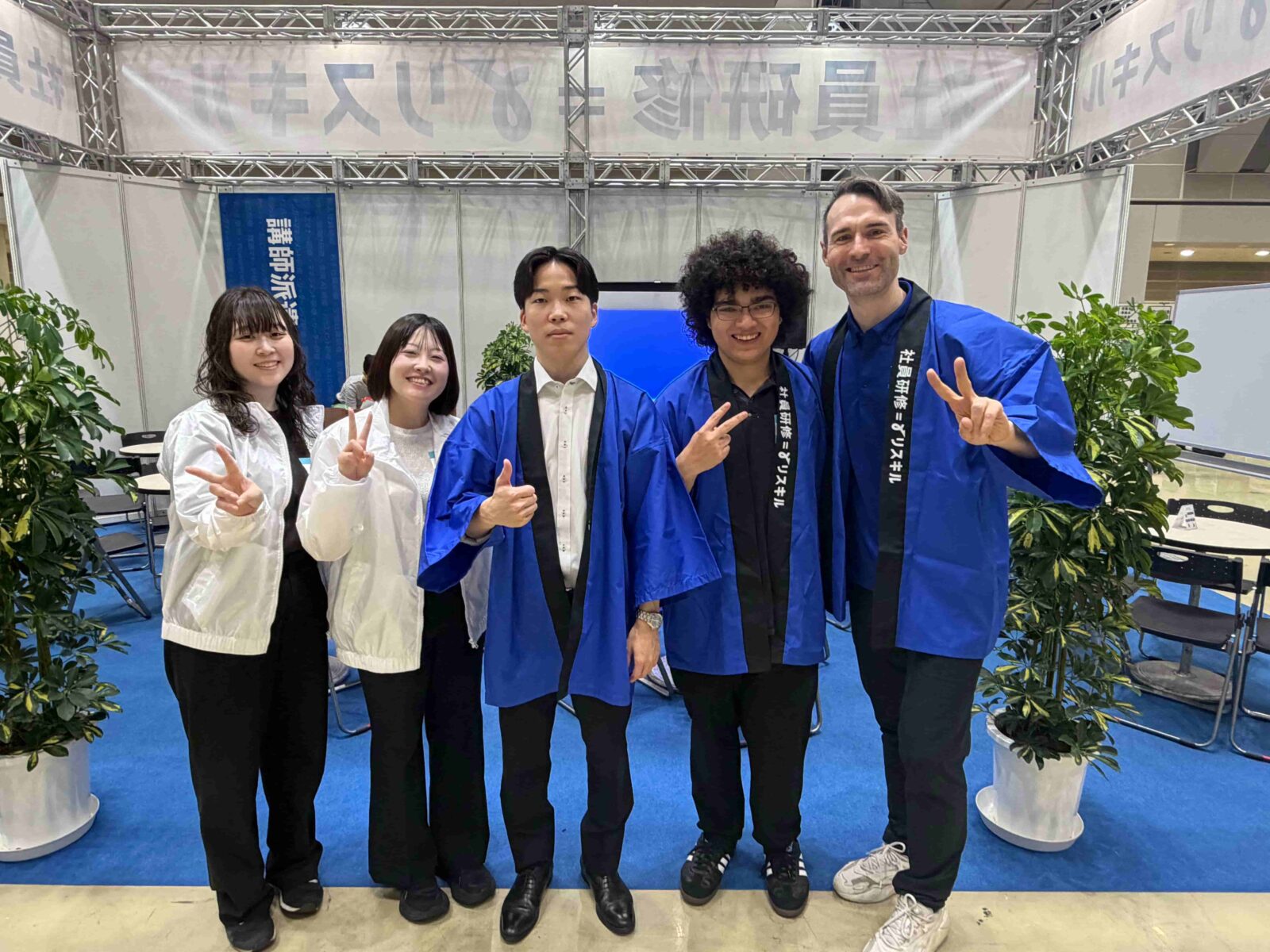 Five people pose for a group photo together. Three of them wear blue robes.