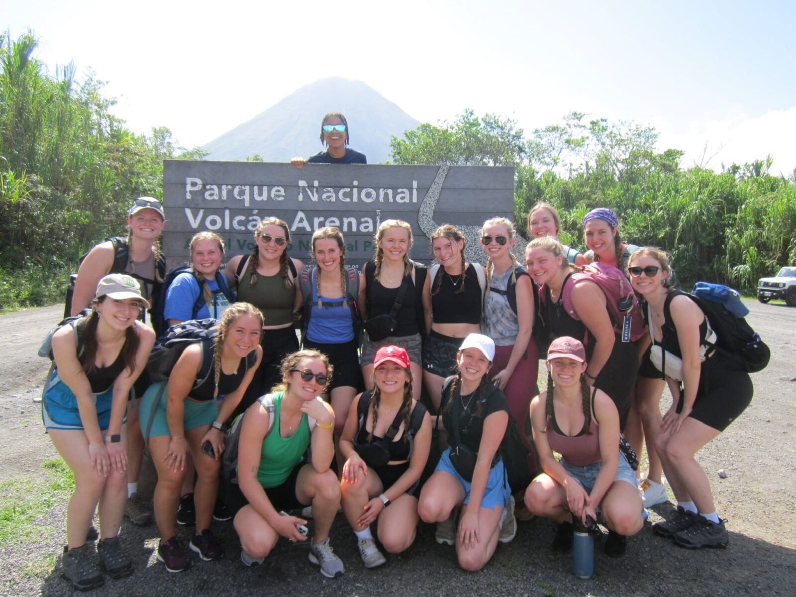 A group of students posing next to a sign that say “Parque Nacional Volcán Arenal”, with a steep mountain in the background.