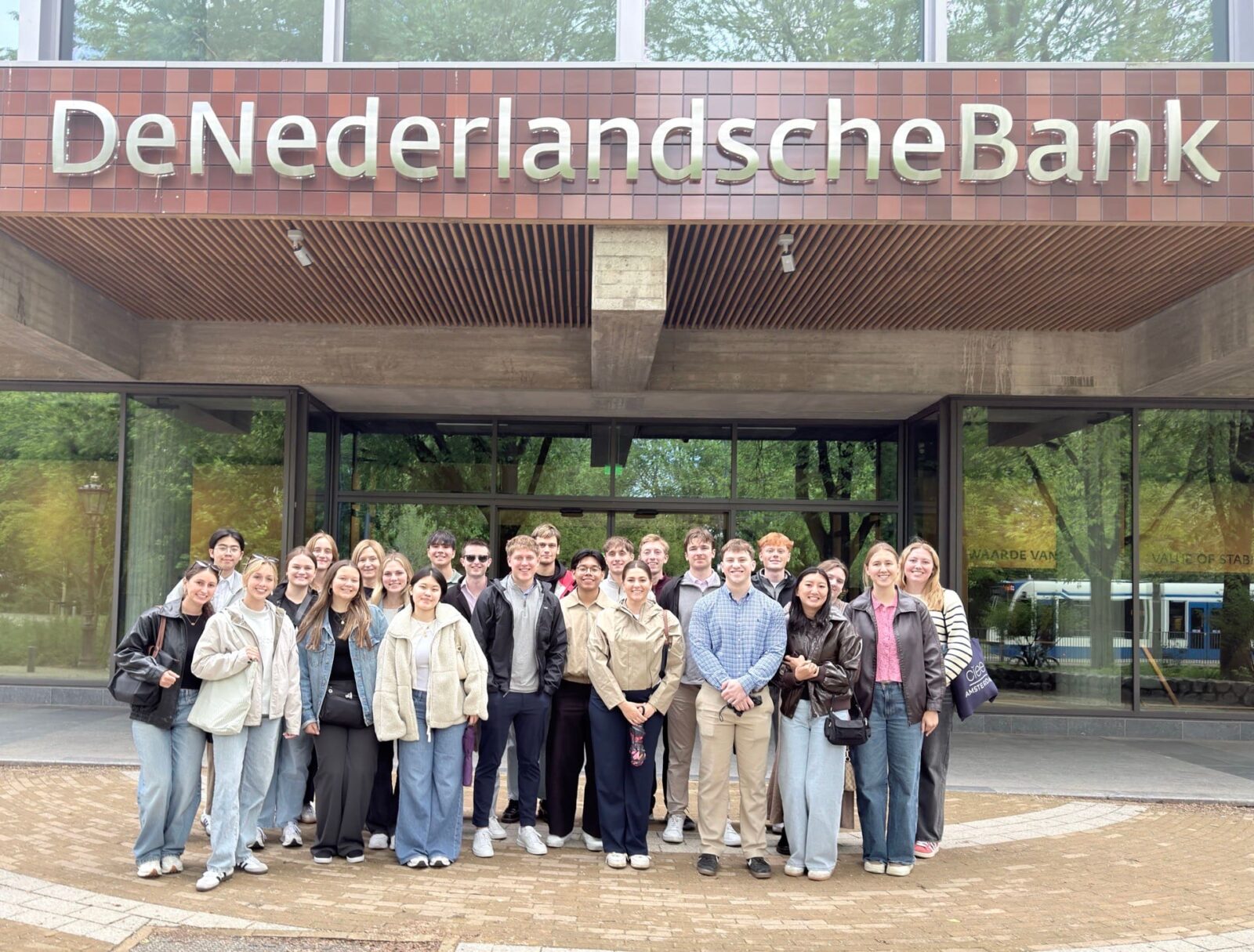 A large group of students outside, posing in front of a building with the entry sign “DeNederlandscheBank”.