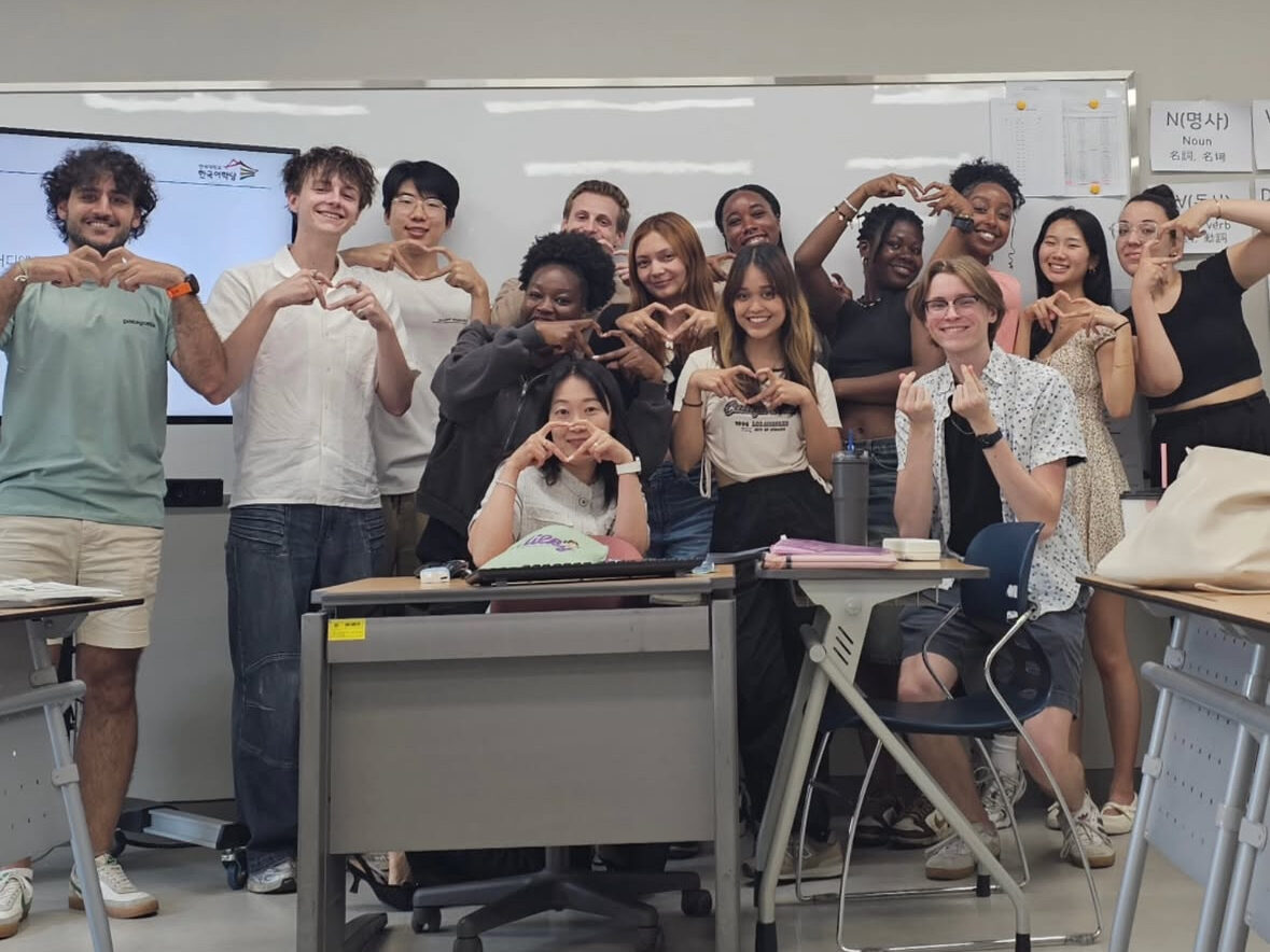 Fourteen students gathered at the front of a classroom, posing for a photo.