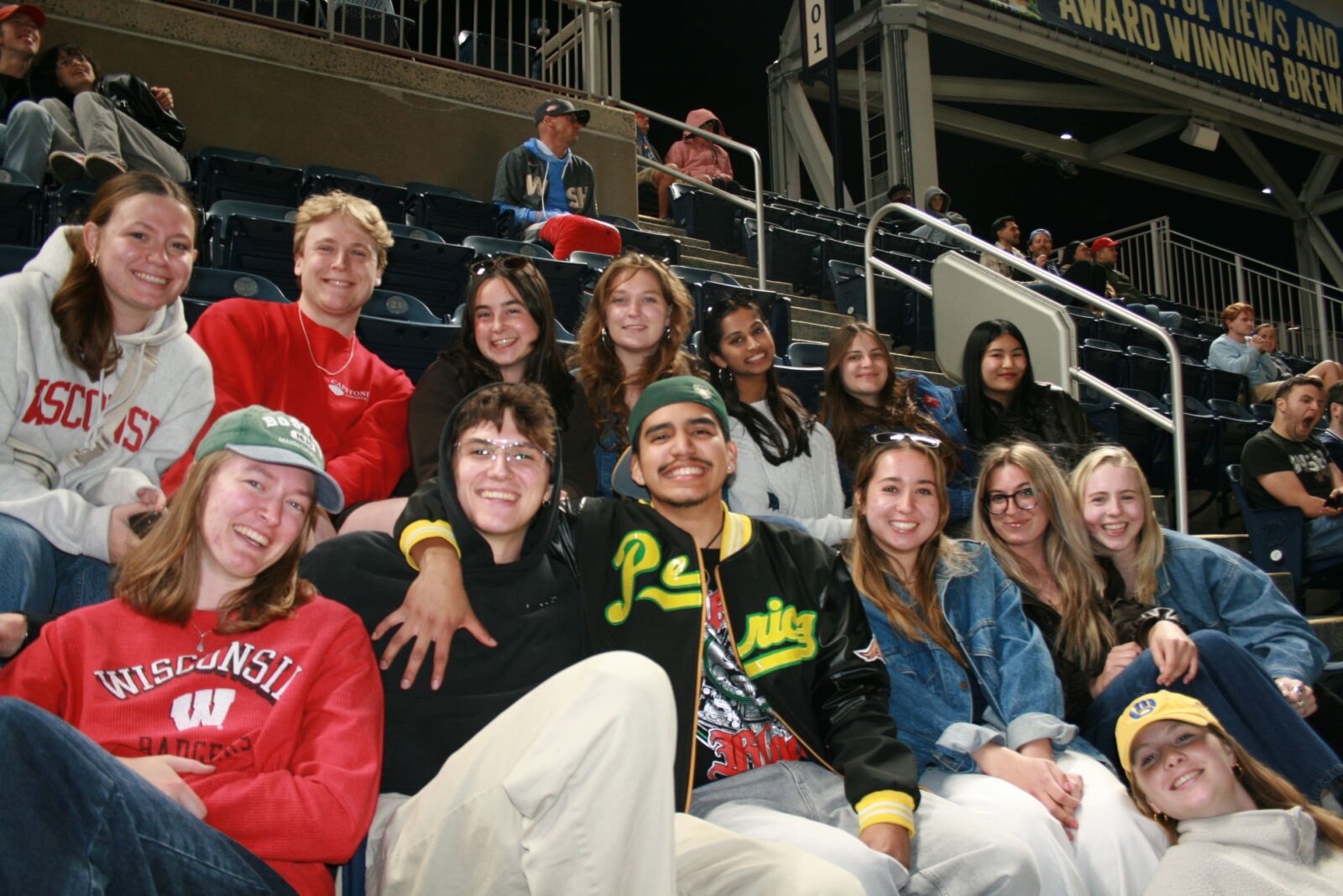 Fourteen students posing in a baseball stadium.