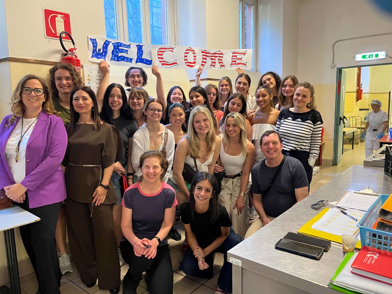Over twenty individuals posing as a group in an industrial interior, with several holding up a sign that reads "Welcome".