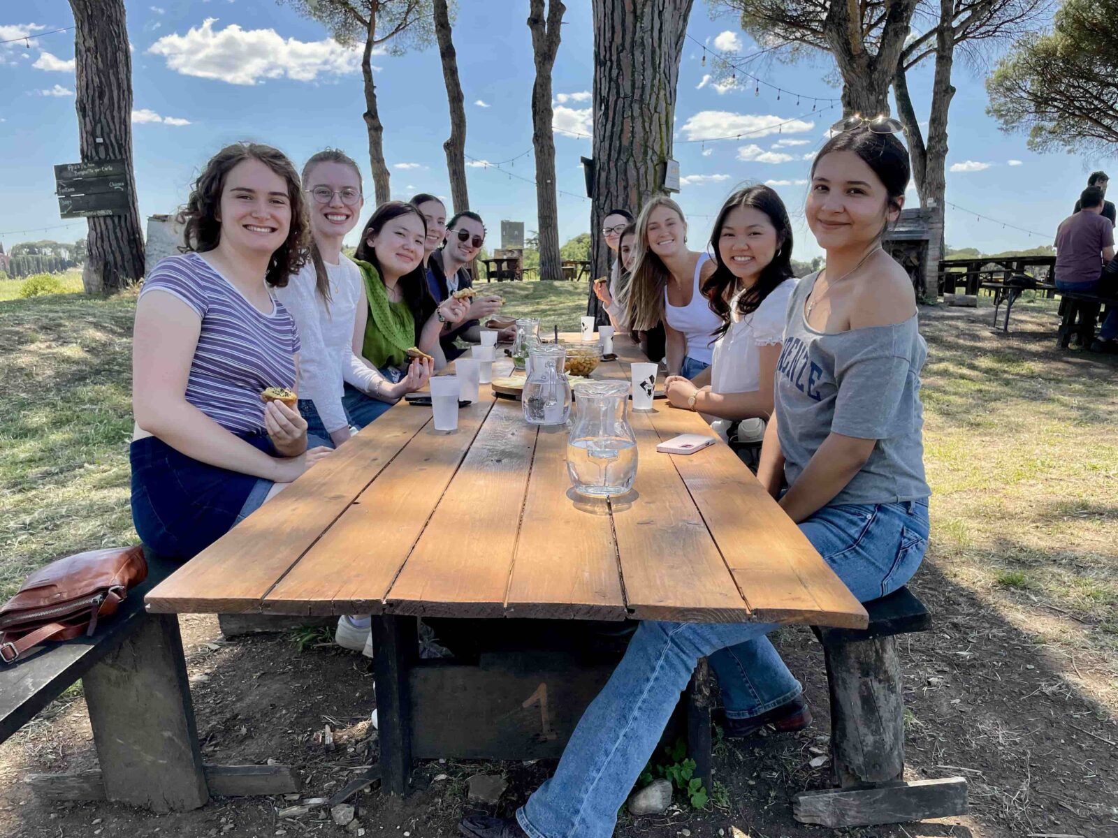 A group of students sitting at picnic table on a sunny day.